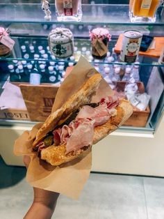 a person holding a sandwich in front of a display case