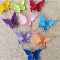 six origami butterflies are arranged in different colors on the floor, with one being folded