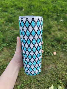 a hand holding up a cup with blue and white designs on it in the grass