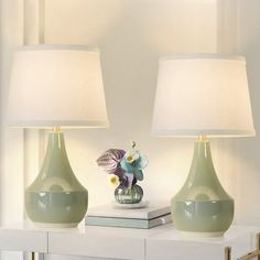 two green vases sitting on top of a white table next to a book and lamp