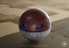 a red and silver ball with blue eyes sitting on top of a cement floor next to a sidewalk