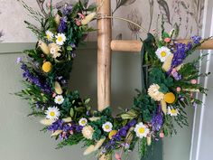 a wreath with flowers and greenery hanging on a wall next to a wooden chair