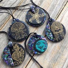 four necklaces with different designs on them sitting on a wooden table next to each other