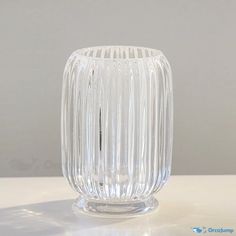 a clear glass vase sitting on top of a white table next to a gray wall