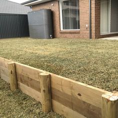 a wooden fence in front of a brick house with grass growing on the ground and around it