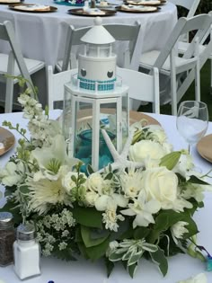 a table topped with white flowers and a light house centerpiece on top of it