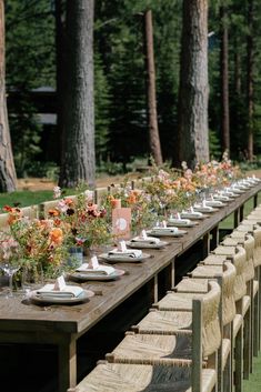 a long table set up with flowers and place settings for an outdoor dinner party in the woods