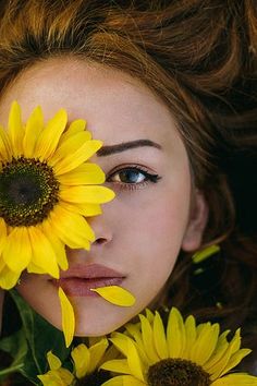 a woman with sunflowers in her hair and eyes looking at the camera while laying down