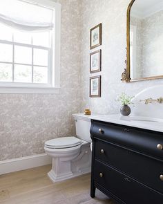 a white toilet sitting next to a black dresser in a bathroom under a large mirror