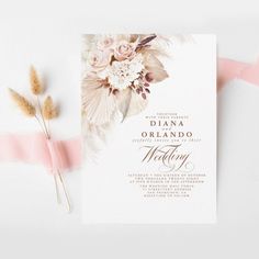 a wedding card with flowers and feathers on it, next to some pink streamers