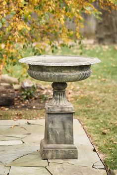 a stone pedestal sitting on top of a cement walkway next to a green leafy tree