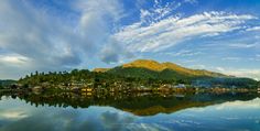 a lake surrounded by mountains and houses under a blue sky with clouds in the background