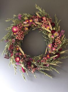 a wreath with pink flowers and green leaves hanging on the wall next to a gray wall