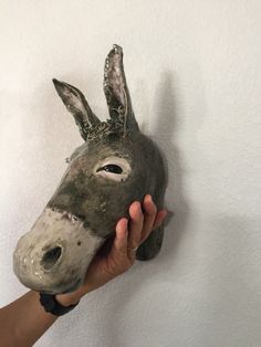 a person holding up a mask shaped like a donkey's head on a wall