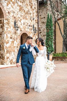 a bride and groom walking in front of a stone building