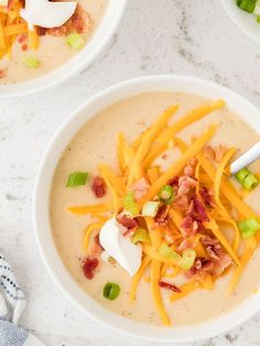 two white bowls filled with soup and topped with cheese, bacon, green onions and scallions