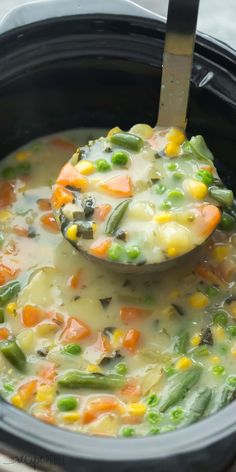 a ladle full of vegetable soup being held by a wooden spoon