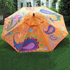 an orange umbrella with paisley designs on it in the grass next to a white house