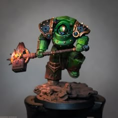 a green and gold painted warhammer holding a glowing fire torch on top of a wooden table