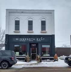 two trucks parked in front of a building with snow on the ground and trees around it