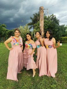 three women in pink dresses posing for the camera with one giving the peace sign and the other holding her hand up