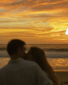 a man and woman standing next to each other on the beach under a sunset sky