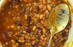 a white bowl filled with chili and beans next to a wooden spoon on top of a table