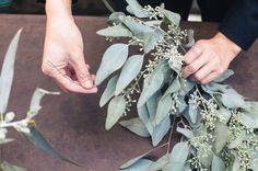 two people are working together to make a floral arrangement with eucalyptus leaves and baby's breath