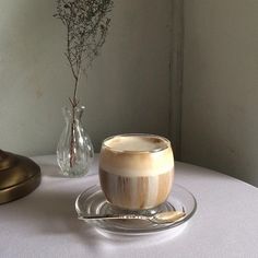 a cup of coffee on a saucer with a spoon next to a vase filled with flowers