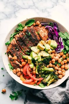 a bowl filled with meat, vegetables and chickpeas on top of a table