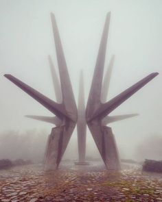 two large metal sculptures sitting on top of a cobblestone ground covered in fog