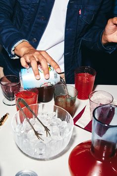 a man is pouring something into a glass at a table with glasses and drinks on it