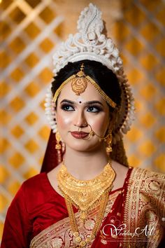 a woman wearing a red and gold bridal outfit with jewelry on her head, posing for the camera