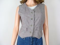 Chic and classic vintage wool tweed fitted waistcoat style vest from the 70s.  The perfect fall and winter layering piece! Features a v neckline with 4 buttons down center front, a sleeveless silhouette with princess seam lines in front and back and two decorative faux pocket flaps on the front sides.  Has pointed hemlines in front and a straight back.  Made of a warm woolen tweed material with small plaid woven designs in shades of gray, off white, black and burgundy.  Freshly laundered and rea 70s Waistcoat, Fitted Waistcoat, Waistcoat Style, Fitted Vest, Tweed Material, Vest Layering, Tweed Vest, Style Vest, Come Undone