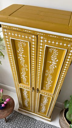 a yellow painted armoire next to potted plants and a planter on the floor