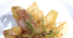 a white plate topped with potatoes and meat covered in seasoning next to a sprig of dill