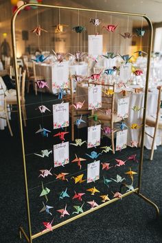 there are many origami cranes on the display rack at this wedding reception, which is decorated with white tablecloths and chairs