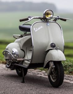 an old scooter is parked on the side of the road near some grass