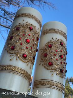 two white vases with red and gold designs on the top, one is tall