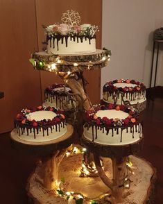 three tiered cake with white frosting and chocolate drips on top sitting on a tree stump