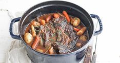 a pot filled with meat and vegetables on top of a white table next to utensils