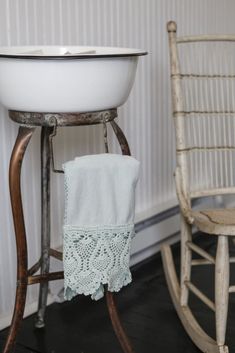 a white sink sitting on top of a wooden stand next to a chair and table