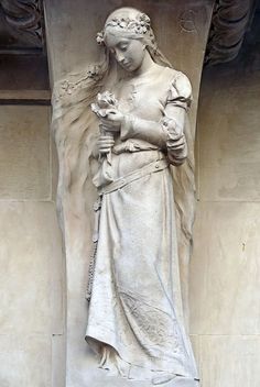 a statue of a woman standing next to a wall with a flower in her hand