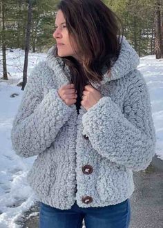 a woman is standing in the snow wearing a gray jacket and jeans with her hands on her hips