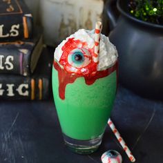 a green drink with eyeballs and strawberries in it on a table next to some books