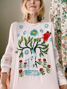 a woman is standing in front of a wall wearing a white shirt with flowers on it