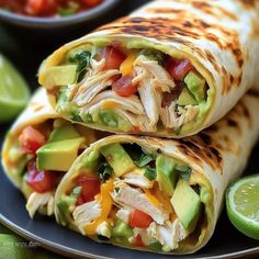 two burritos on a plate with avocado, tomato, and chicken