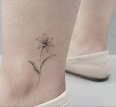 a small flower tattoo on the side of a woman's leg, with her foot