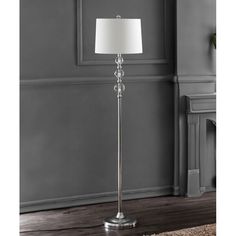 a floor lamp with a white shade on the top and silver base, in front of a