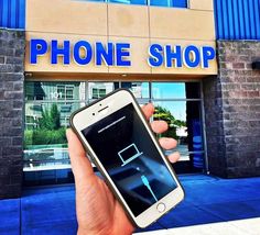 a person holding up a cell phone in front of a building with the words phone shop on it